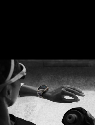 Eine Joggerin blickt auf die Apple Watch Ultra 2 am linken Handgelenk und macht die Doppeltipp Geste mit Zeigefinger und Daumen der linken Hand.