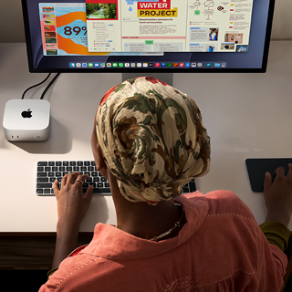 Eine Person tippt an einem Schreibtisch mit einem Mac mini, Studio Display angeschlossen, Magic Keyboard, Magic Trackpad, verschiedene Objekte